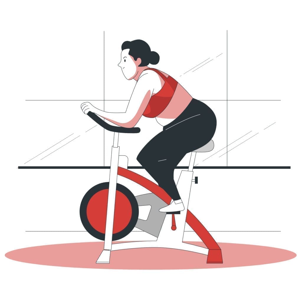 A person is exercising on a stationary bike, wearing a red sports bra and black leggings. They are focused and leaning forward slightly, gripping the handlebars. The bike features a red wheel and a white frame. The background includes large windows, suggesting a bright indoor environment. A soft red oval shape is beneath the bike, adding a touch of color to the scene.