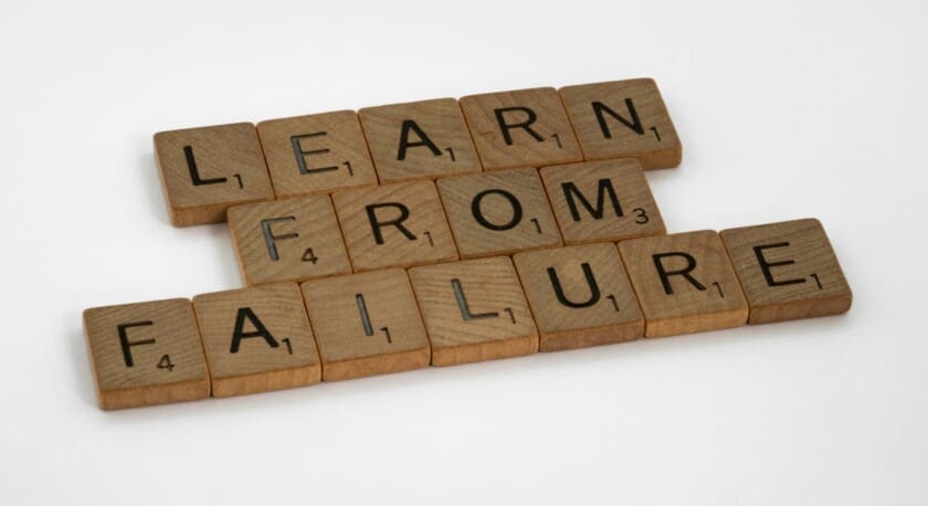 Wooden letter tiles arranged to spell "LEARN FROM FAILURE." Each tile features a letter in a bold font, with some tiles indicating point values, suggesting a connection to a word game. The background is plain white, emphasizing the simplicity and clarity of the message.