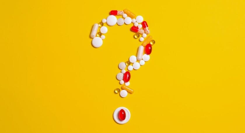 A variety of pills and capsules are arranged to form a question mark on a bright yellow background. The assortment includes white tablets, red and yellow capsules, and a few gel capsules, creating a visually striking contrast against the vibrant backdrop.