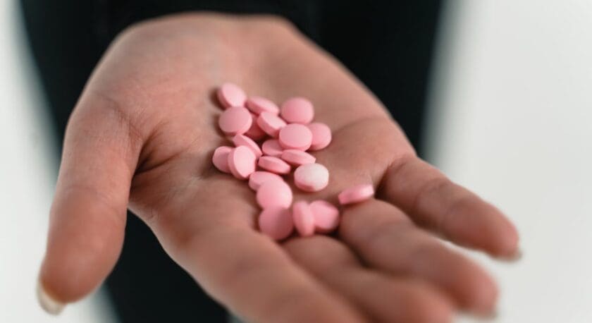 A hand holding a small pile of round pink tablets or pills.