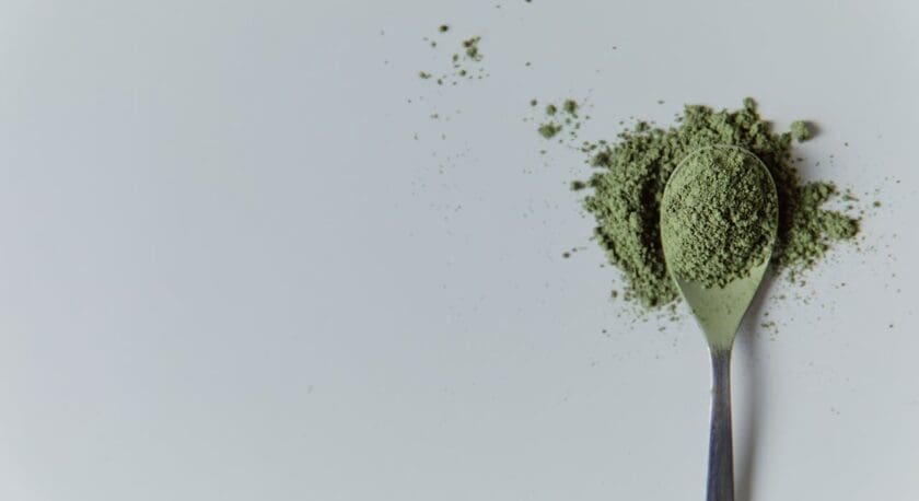 A metal spoon filled with green powder, with some of the powder spilled around it on a white surface.