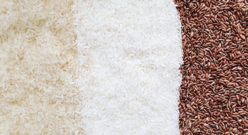 Three types of rice grains arranged side by side: light brown rice on the left, white rice in the center, and red rice on the right.