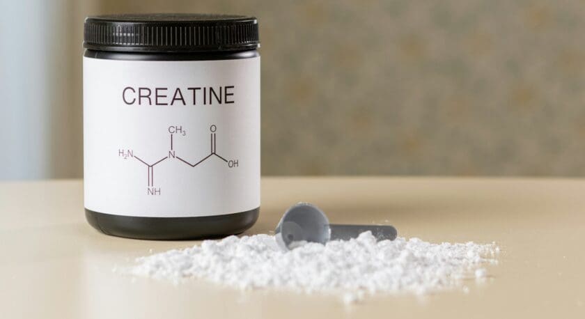 Black container labeled "CREATINE" with a chemical structure diagram on the front, next to a pile of white powder and a gray scoop on a beige surface.