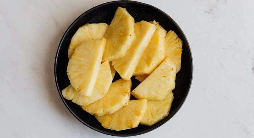 Sliced pineapple pieces arranged in a black bowl on a white marble surface.