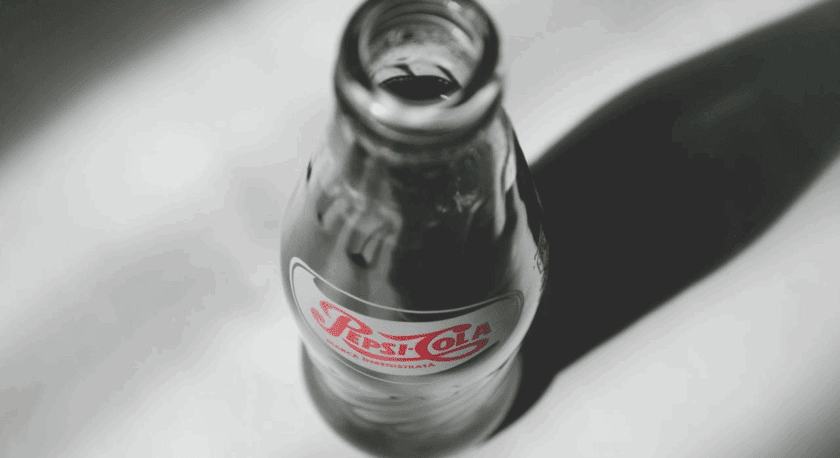 Glass bottle of Pepsi-Cola with a vintage-style label, viewed from above on a light surface casting a shadow.